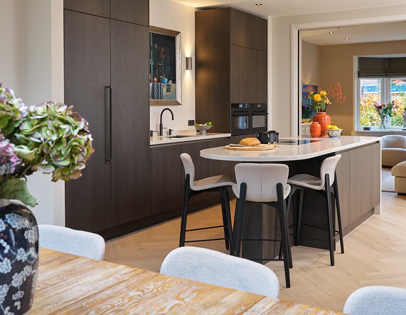 Donkerbruine-houtlook-keuken-met-kookeiland-en-afgerond-werkblad-met-bar